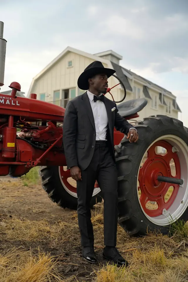 Kobe Apponsah, founder of Summit Customs, in a black tuxedo and western hat beside a red vintage tractor